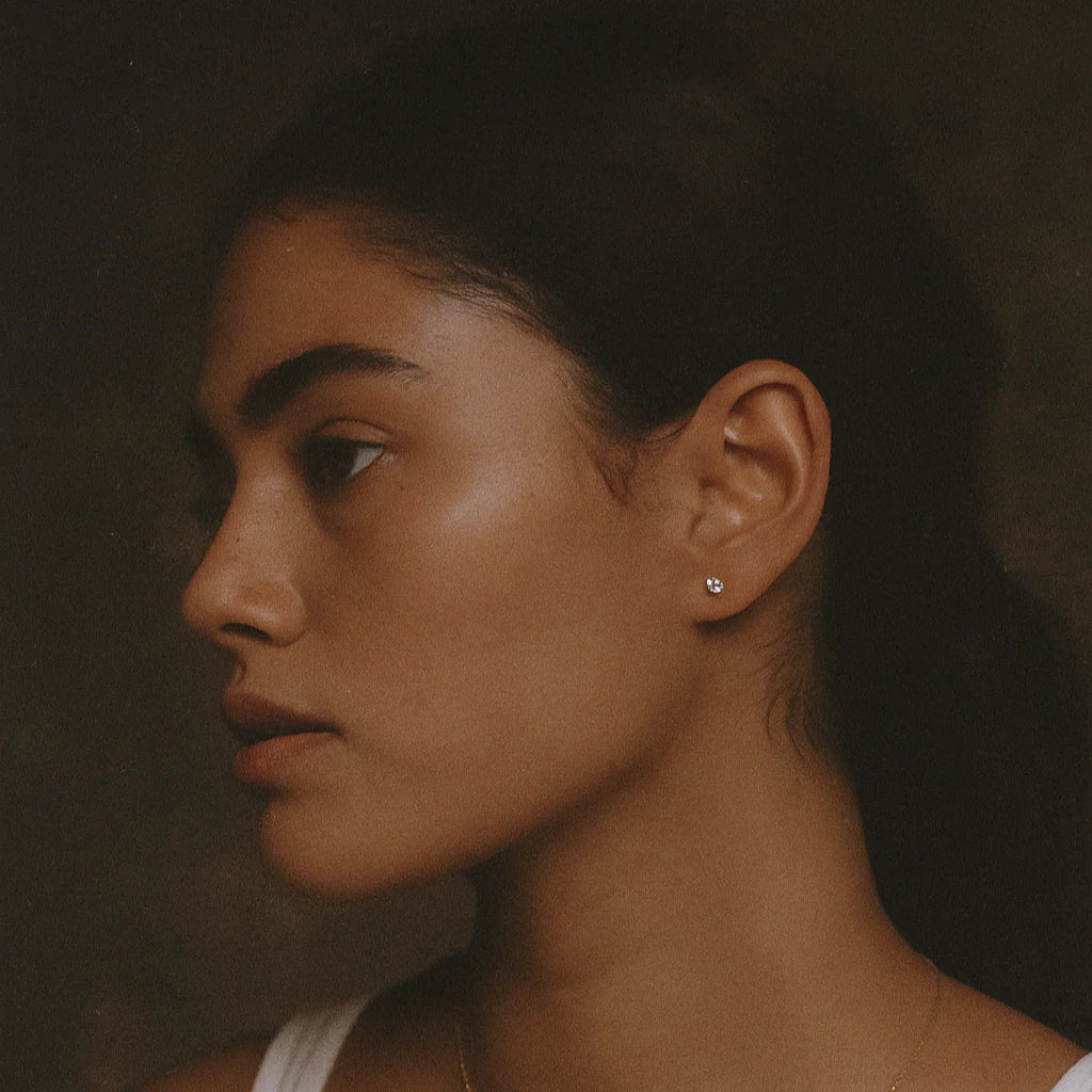 Side profile of a person with dark hair and minimal makeup against a dark background